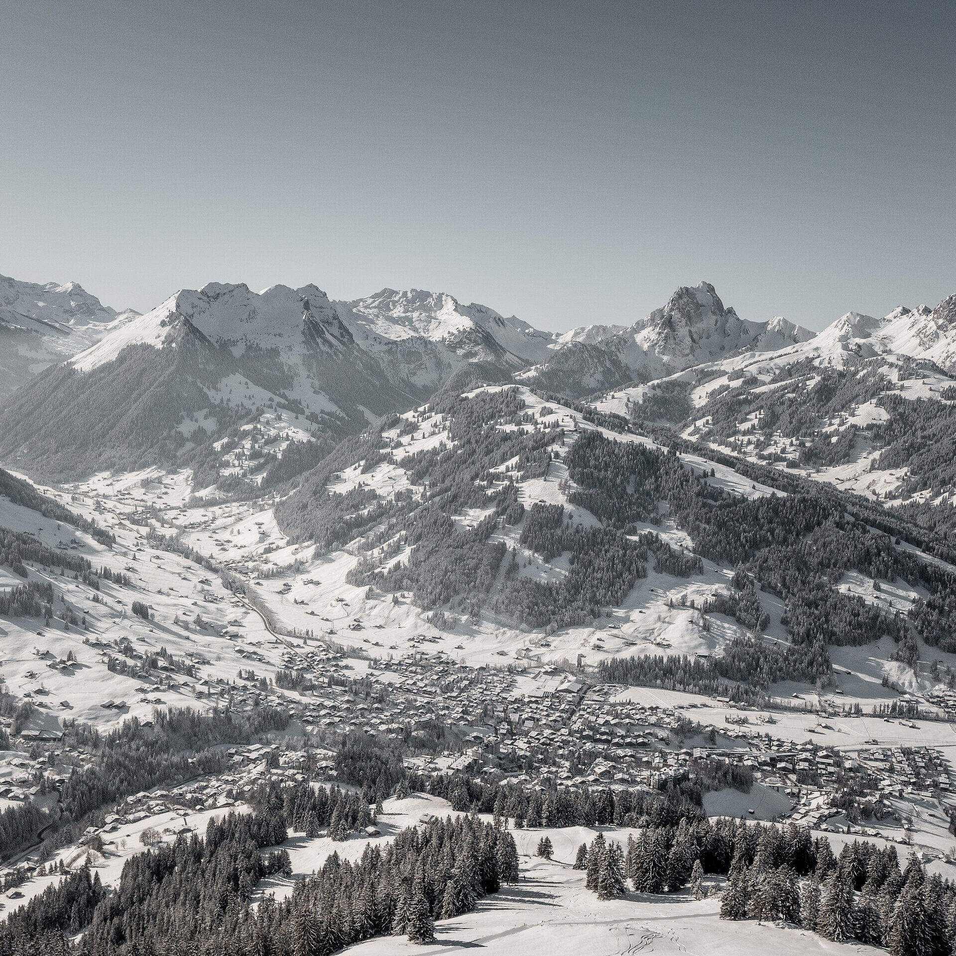 Panoramablick auf das winterliche Dorf Gstaad mit dem Berg Eggli sowie weiteren Bergen im Hintergrund.