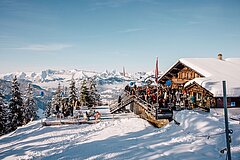 Eine Gruppe von Menschen auf einer Terrasse im Schnee neben einem Bergrestaurant.