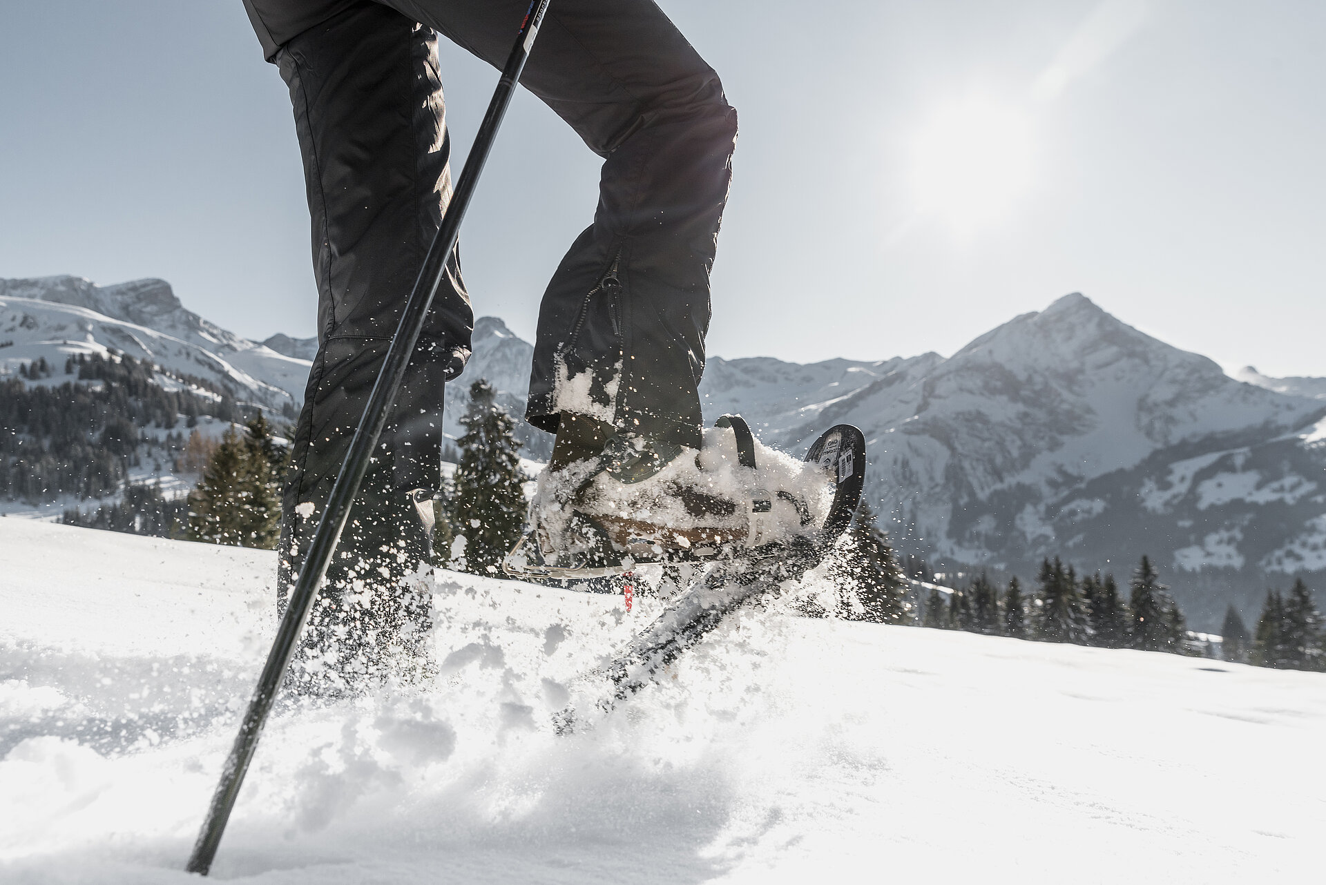 Männliche Beine welche mit Schneeschuhschuhen durch den Schnee stampfen vor herrlicher Bergkulisse.