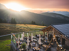 Ein Bergrestaurant im Sonnenuntergang mit Gästen auf der Terasse.