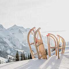 Drei hölzerne Schlitten stehen zuoberst auf dem Berg im frischen Pulverschnee. Im Hintergrund weisse Berggipfel.