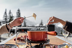  Red fondue caquelon with two people’s hands eating cheese fondue.