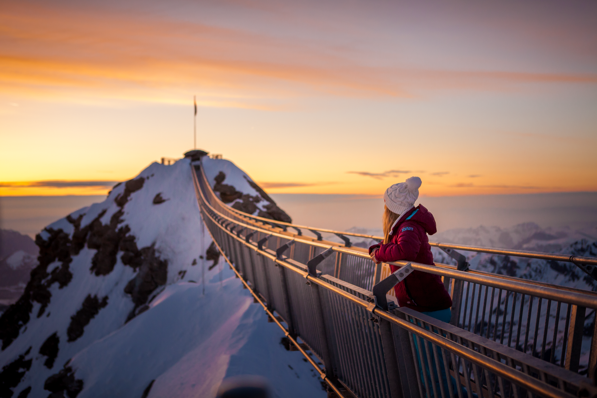 Eine Frau, welche auf der Hängebrücke auf dem Glacier 300 steht und den Sonnenuntergang betrachtet.