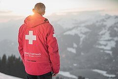 Dressed in a red jacket, Walter Reichenbach looks out over the distant winter landscape.
