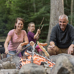 Familie mit zwei Kinder grilliert am Feuer Cervelats und Schlangenbrot.