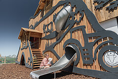 Eine Mutter betrachtet mit ihrem Kleinkind den Fassadenspielplatz am Berghaus Rinderberg