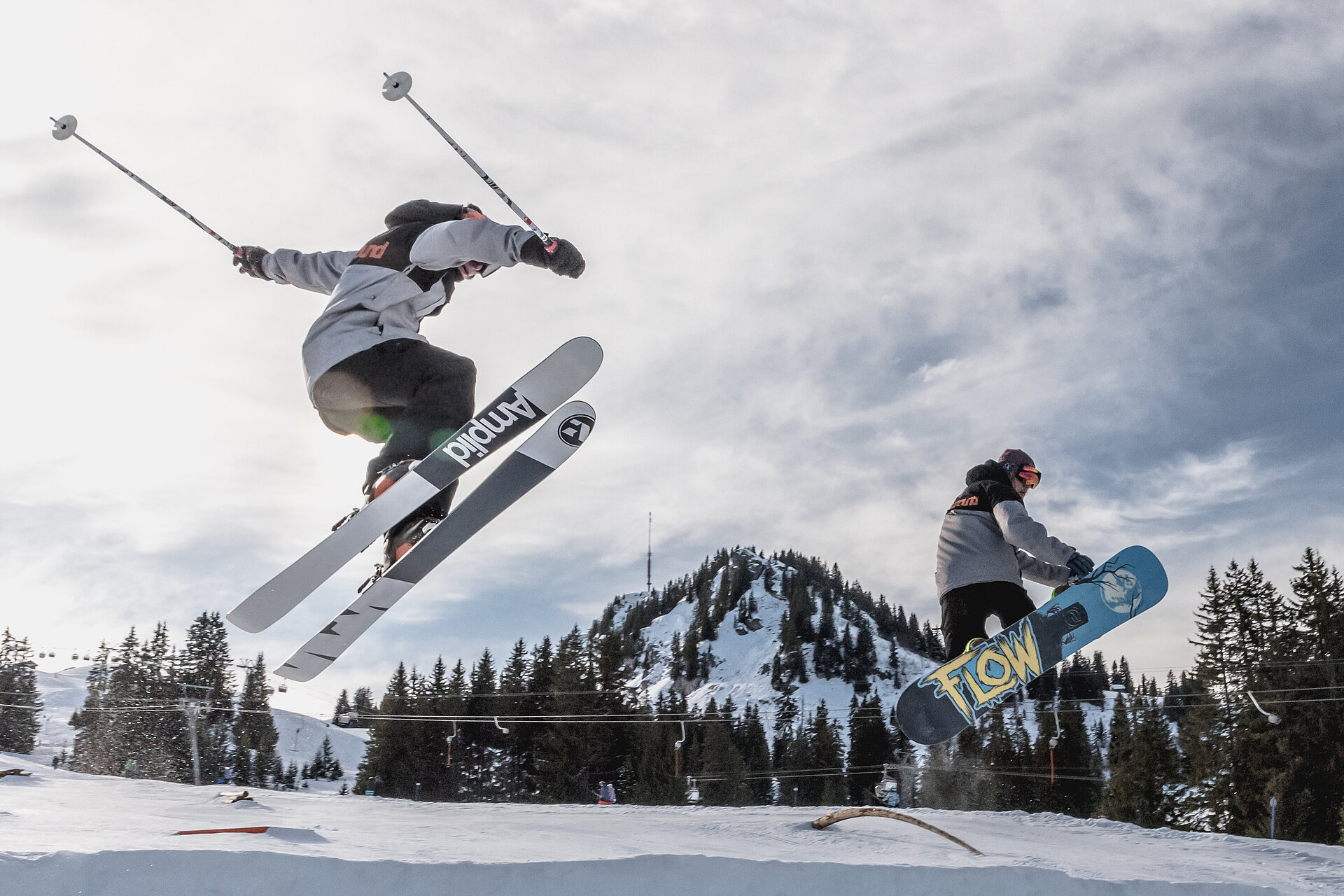 Ein Skifahrer und ein Snowboarder beim Üben von Kunststücken im Snowpark in Saanenmöser.