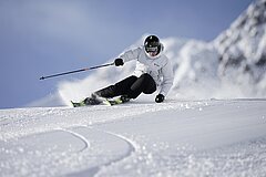 A skier is riding on a snowy slope. The surroundings are mountainous and the sky is clear.