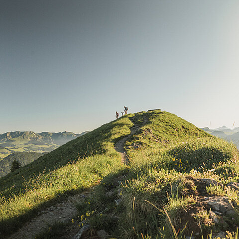 Ein Hügel vor einer Berglandschaft mit einer Familie darauf.