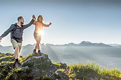 Eine Frau balanciert über einen grossen Stein und ein Mann stützt sie mit der Hand.