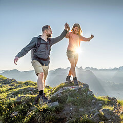 Eine Frau balanciert über einen grossen Stein und ein Mann stützt sie mit der Hand.